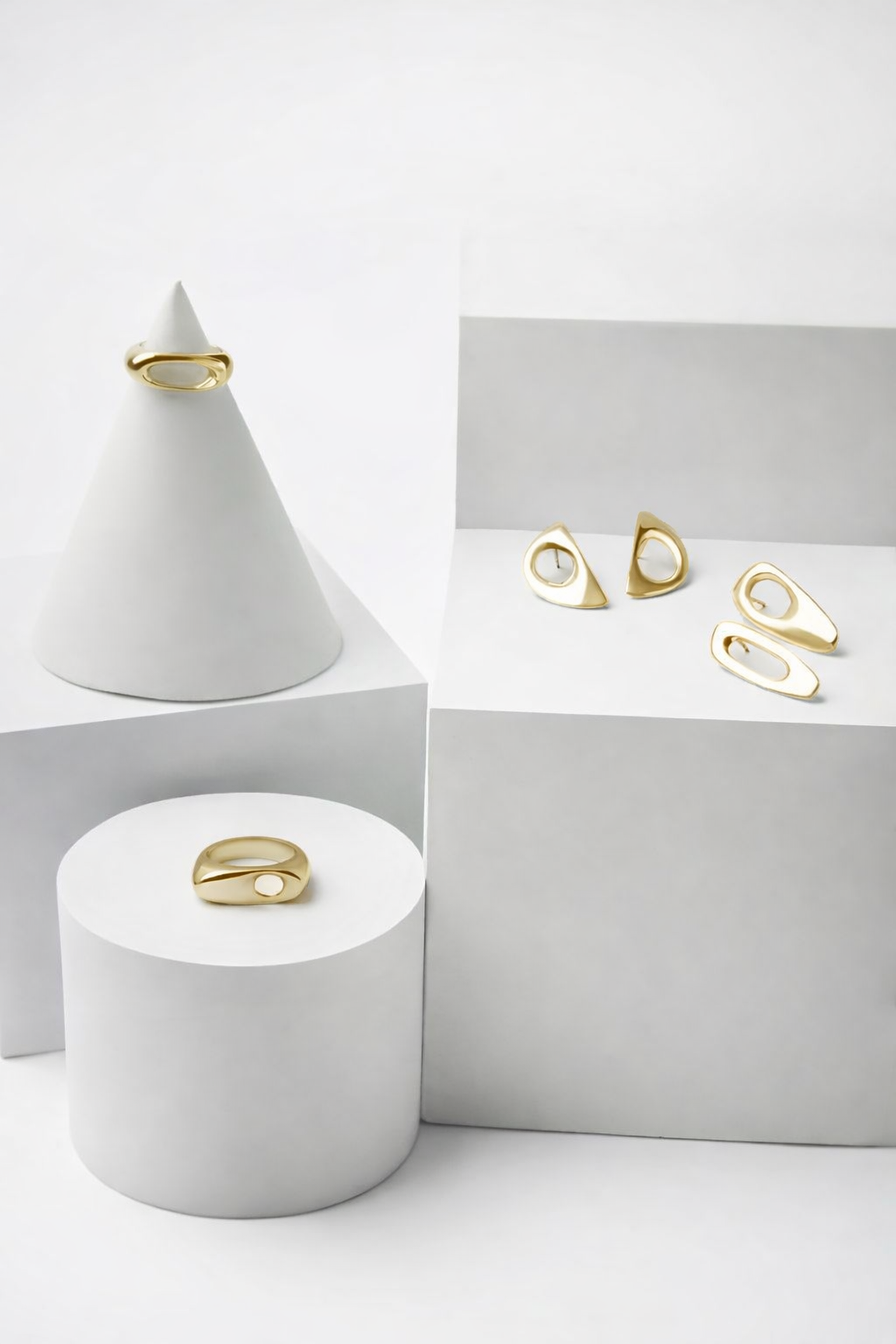 Solid gold sculptural jewelry on white cylindrical and conical stands against a white background